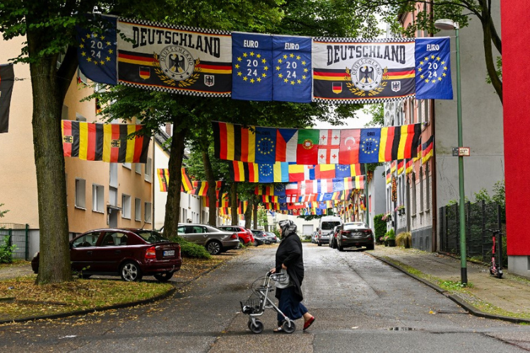 Une femme passe sous des drapeaux exposés dans la Rullichstrasse à Essen, le 4 juillet 2024, lors du Championnat d'Europe de football UEFA 2024.